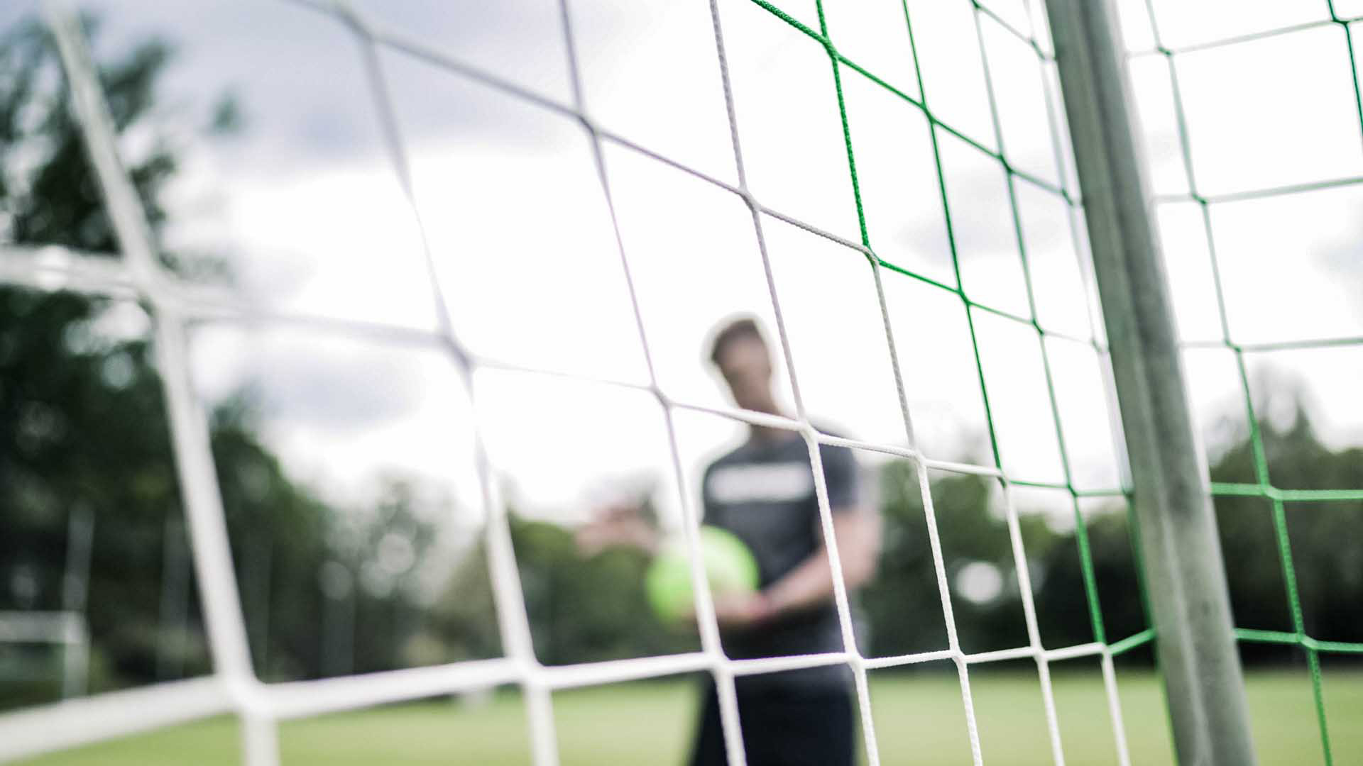 Fußballspieler der hinter einem Tor nachdenklich vom Spielfeld geht.